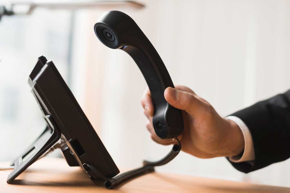 Mano che solleva la cornetta di un telefono da ufficio